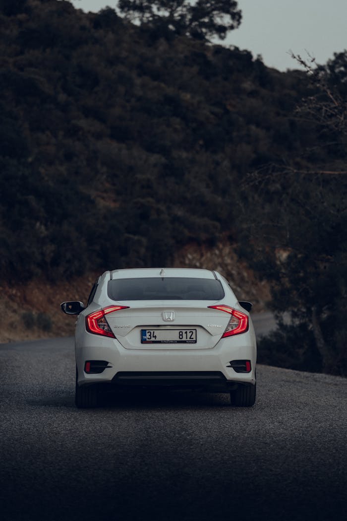 heros-img A white car on a winding road surrounded by dense forest, captured in daylight.